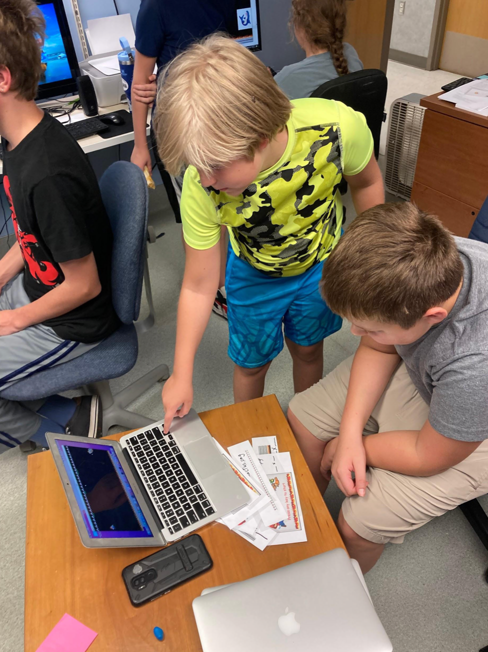 A group of young boys are looking at a laptop on a table
