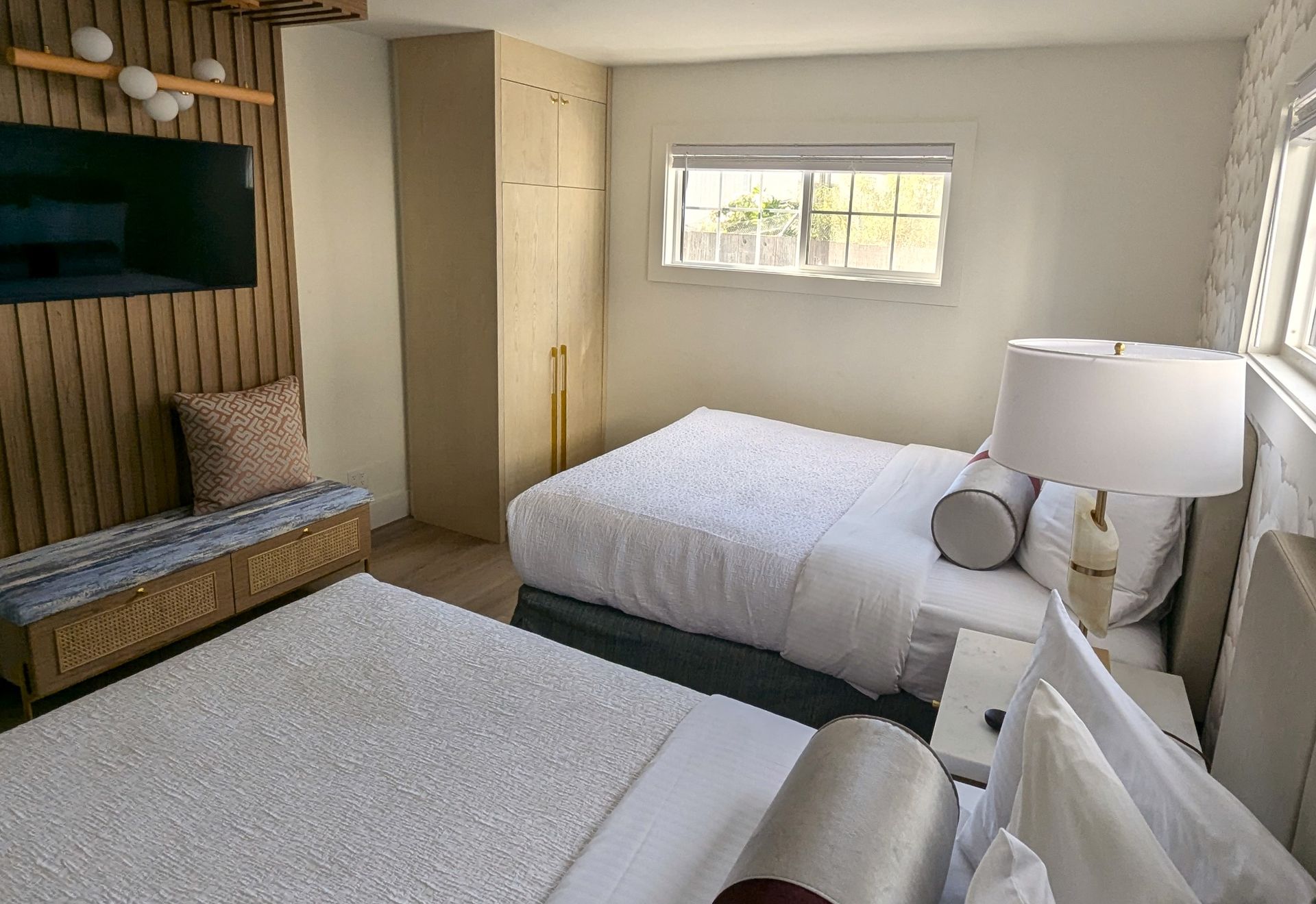 two queen beds and part of a TV with a window in the background