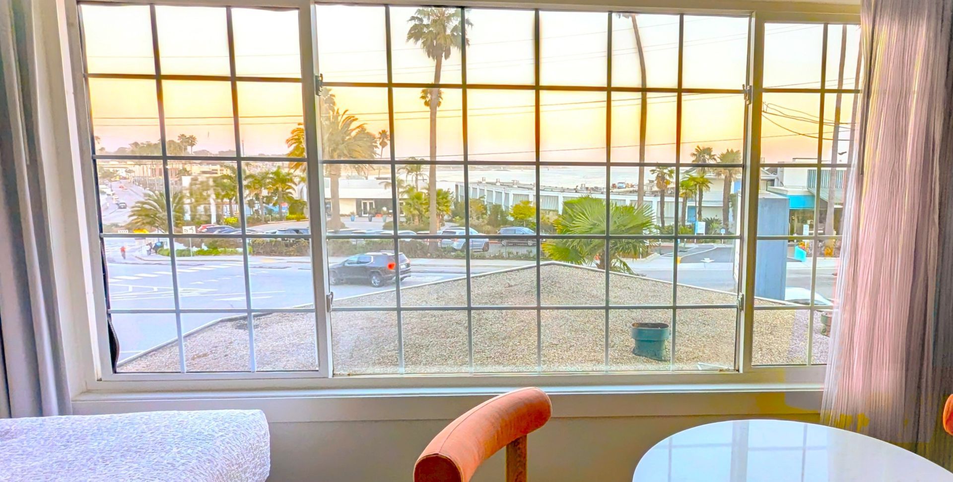 Table in and chairs in front of open window with view of the ocean at sunset