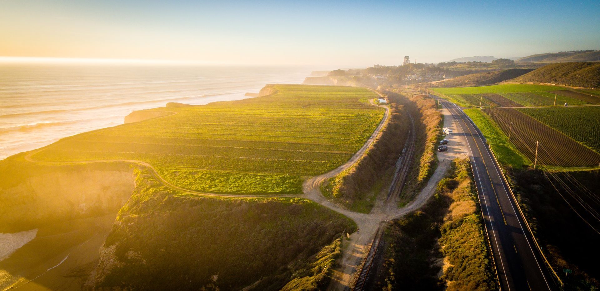 road surrounded by grassy fields with the ocean off to the left