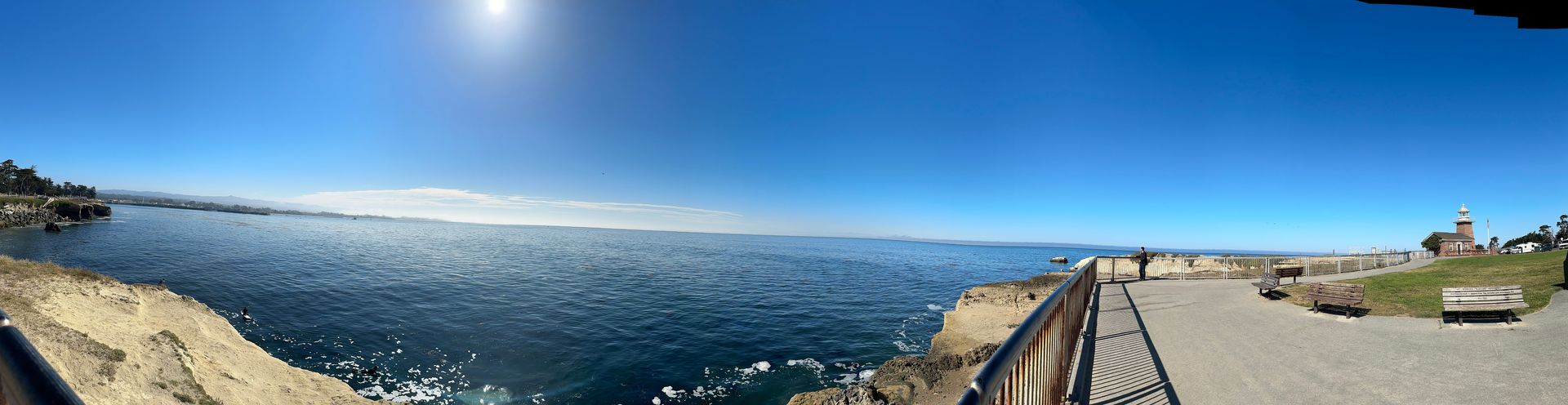 Sun shining above the ocean to the left and a guardrail along a pedestrian walkway to the right