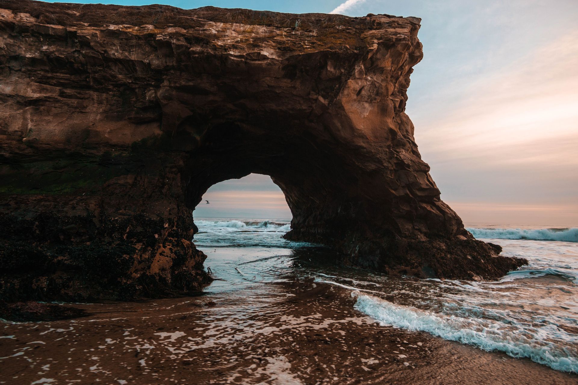 Close up of natural bridge rock formation at local beach with waves lapping near its base