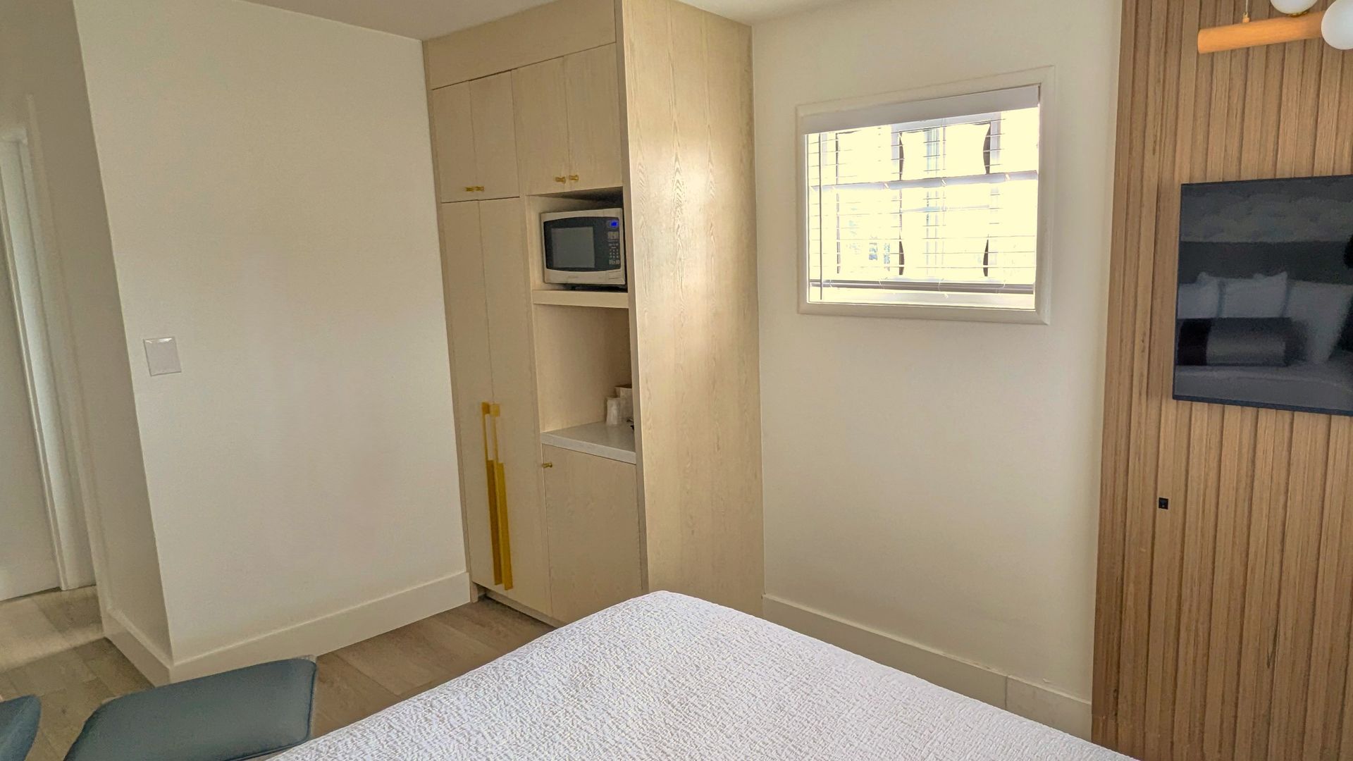 Corner of bed in front of window with microwave on the left and TV to the right