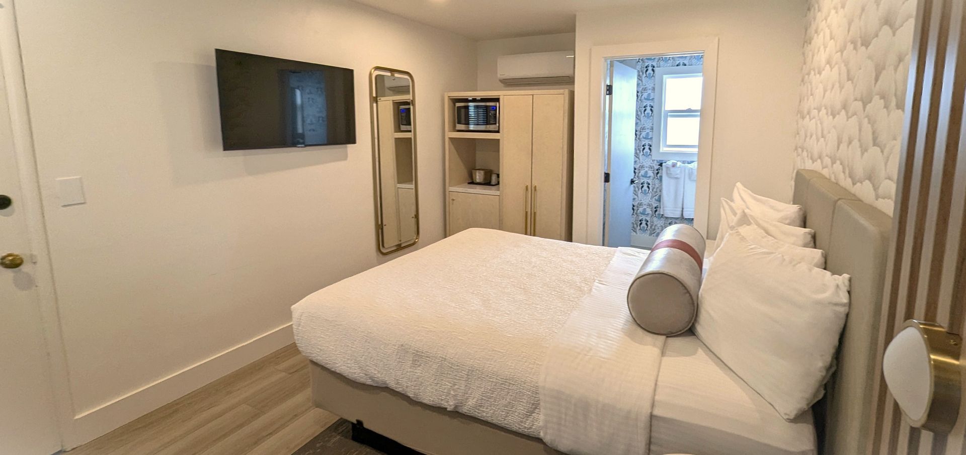 Bed in front of open bathroom door with TV and wardrobe to their left