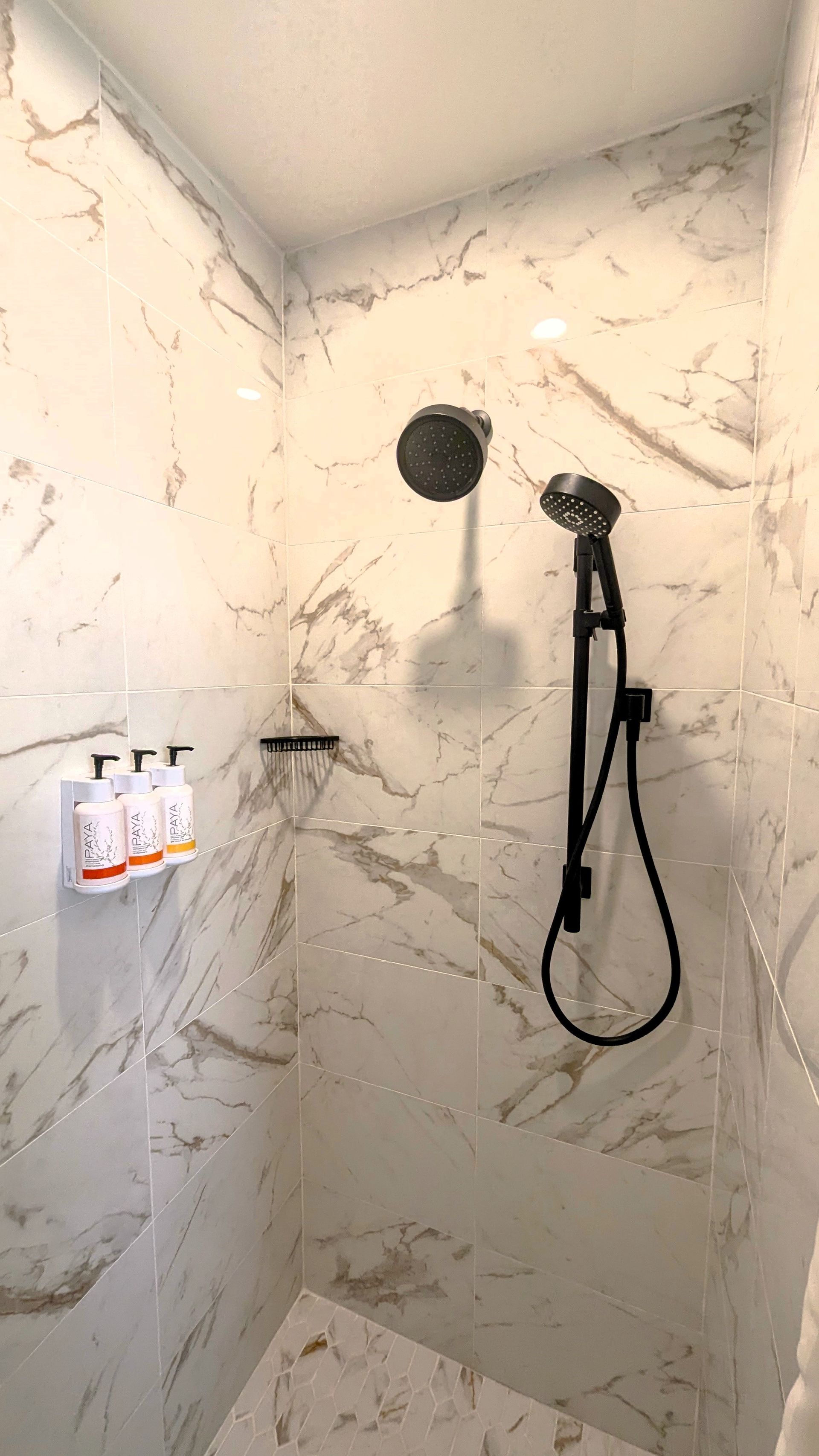 Inside of shower with black fixtures and a white wall-mounted soap dispenser