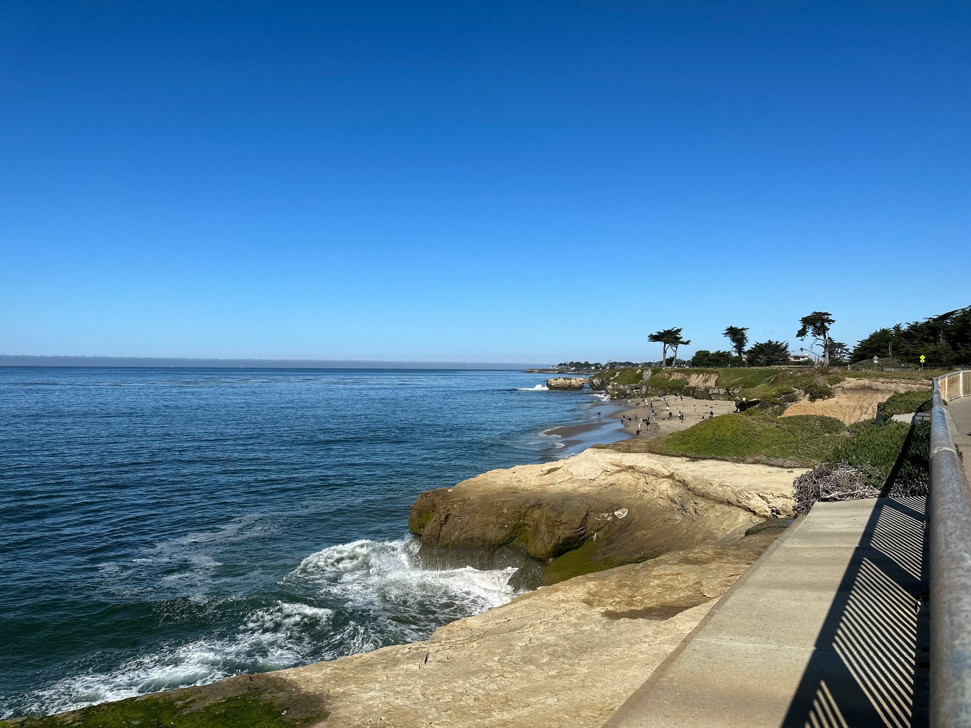 Cliffs above the ocean with a beach full of people on it in the background