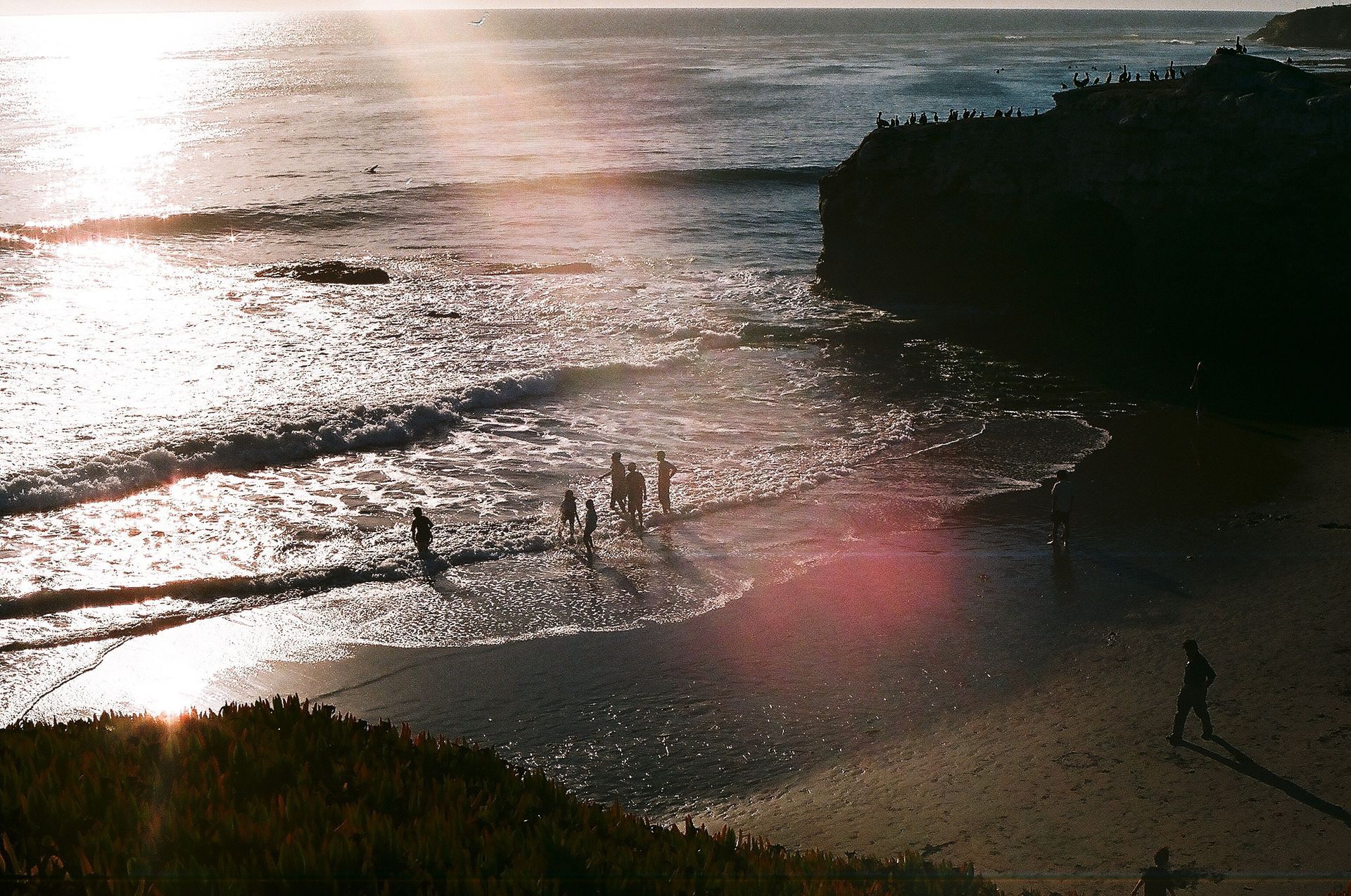 beach surrounded by cliffs with people near the waves close to the shore