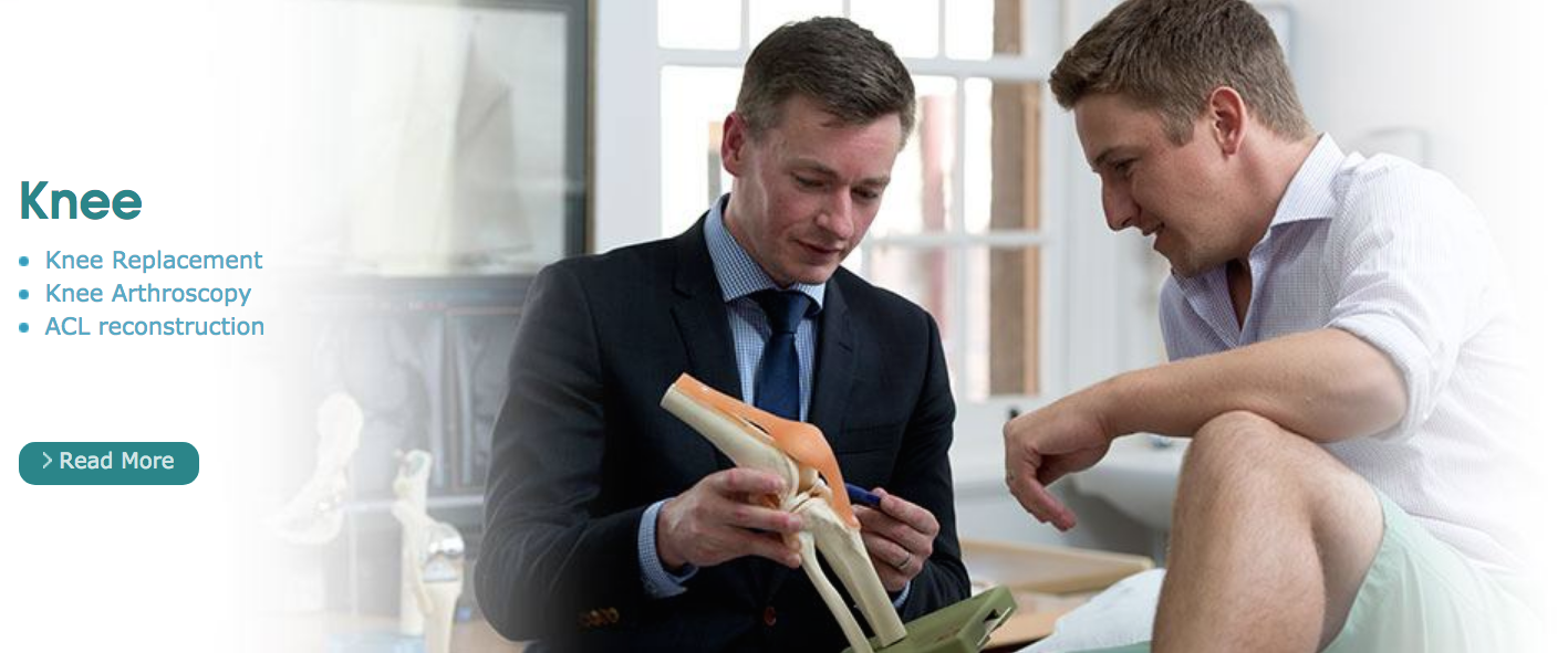 Two men are looking at a model of a knee joint.