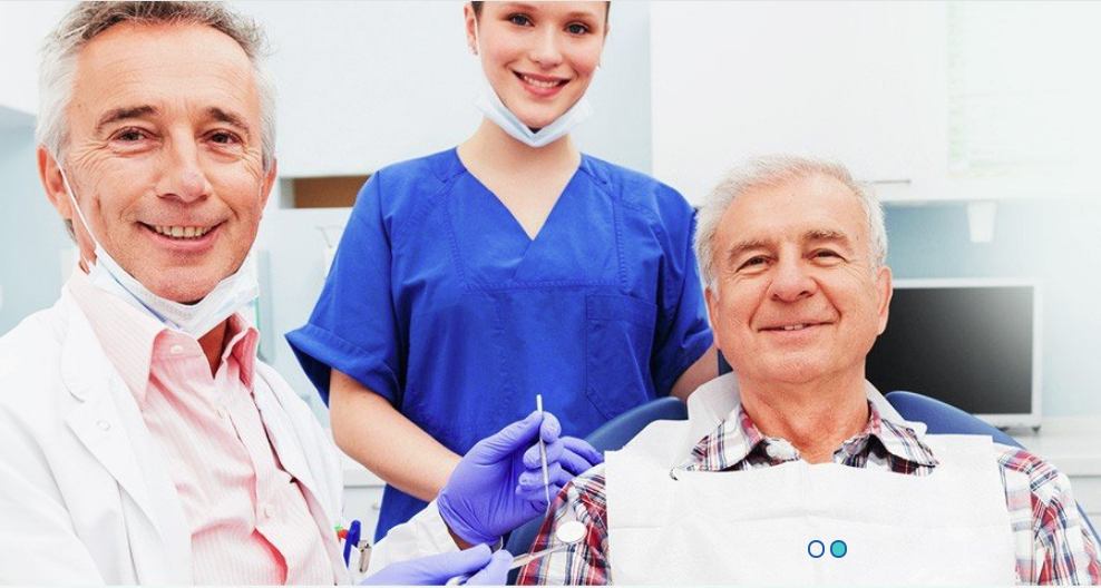 A man is sitting in a dental chair with two dentists and a nurse.