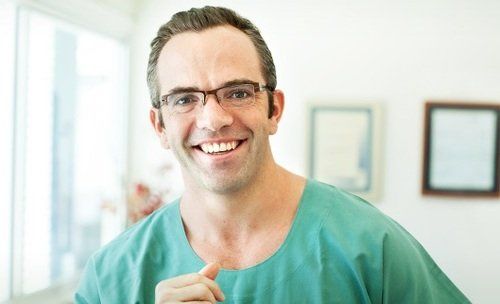 A man wearing glasses and a green scrub is smiling for the camera.