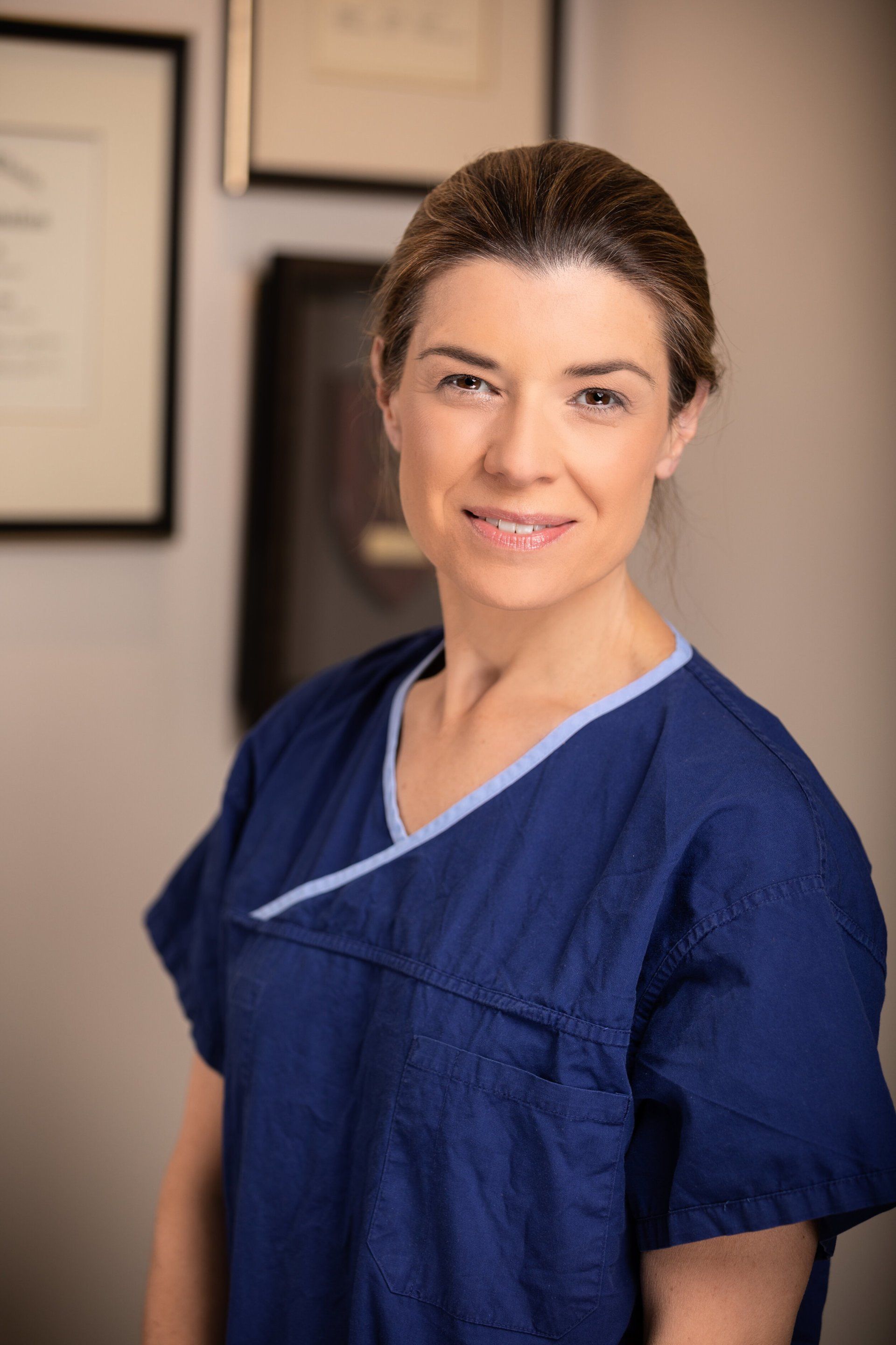 A woman in a blue scrub top is smiling for the camera.