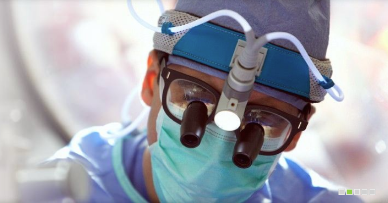 A close up of a surgeon wearing a mask and magnifying glasses