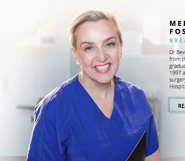 A woman in a blue scrub is smiling and holding a clipboard