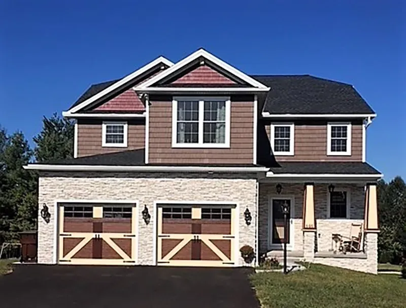 Two-story suburban house with a stone facade, two-car garage, and dark brown wood-paneled upper levels under a clear sky.