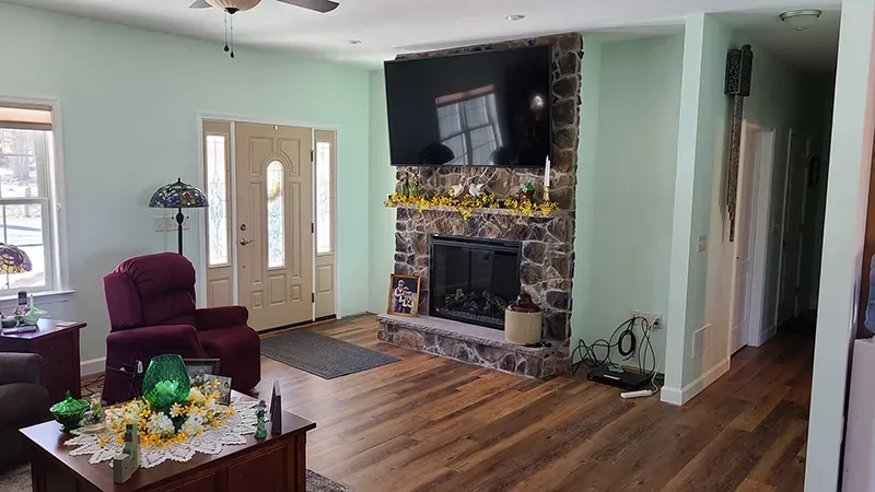 A living room featuring a stone fireplace with a mounted television, a burgundy recliner, and a wooden coffee table.