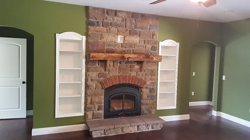 A fireplace with stone masonry and a wooden mantel, flanked by built-in white arched bookshelves in a green-walled room.