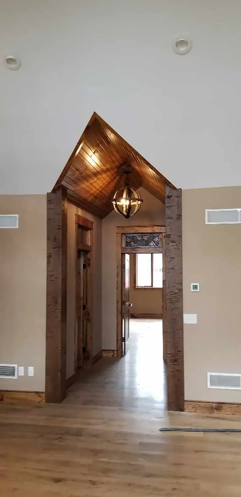 A wood-framed entryway with a peaked, wood-paneled ceiling and pendant light leading into a hallway.