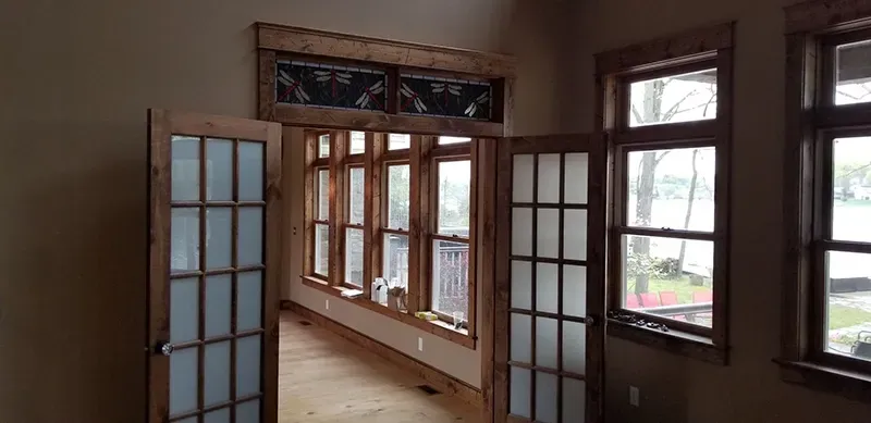 A room with wooden-framed French doors, windows with a lake view, and decorative stained-glass transoms above the doorway.