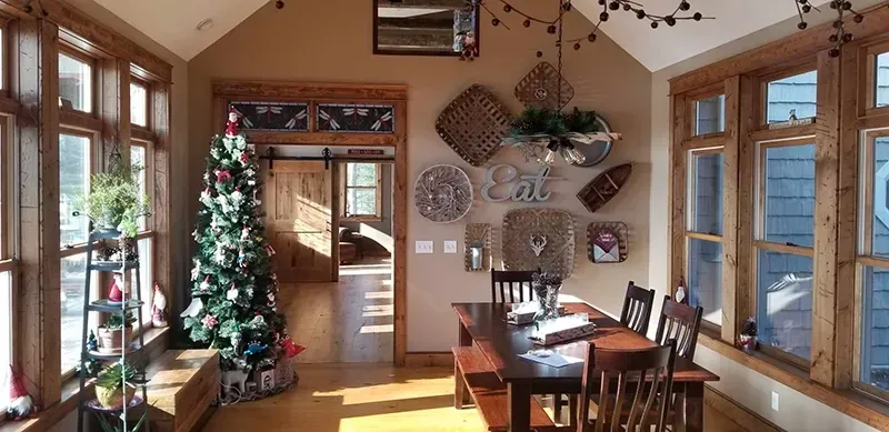 A dining area with a Christmas tree to the left, a wooden table with chairs, and wall-mounted baskets and decor.