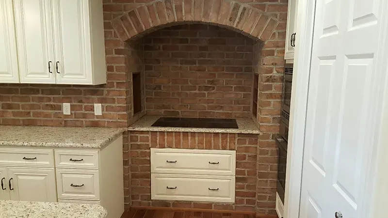 A kitchen featuring a brick-encased stove alcove with an arched top, white cabinets, and speckled granite countertops.