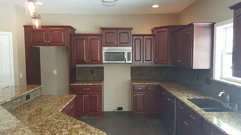 A kitchen with dark cherry wood cabinets, speckled granite countertops, a built-in microwave, and a stainless steel sink.