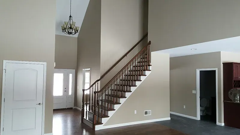 An entryway with a wooden staircase, beige walls, hardwood floors, a white door, and a hanging chandelier.