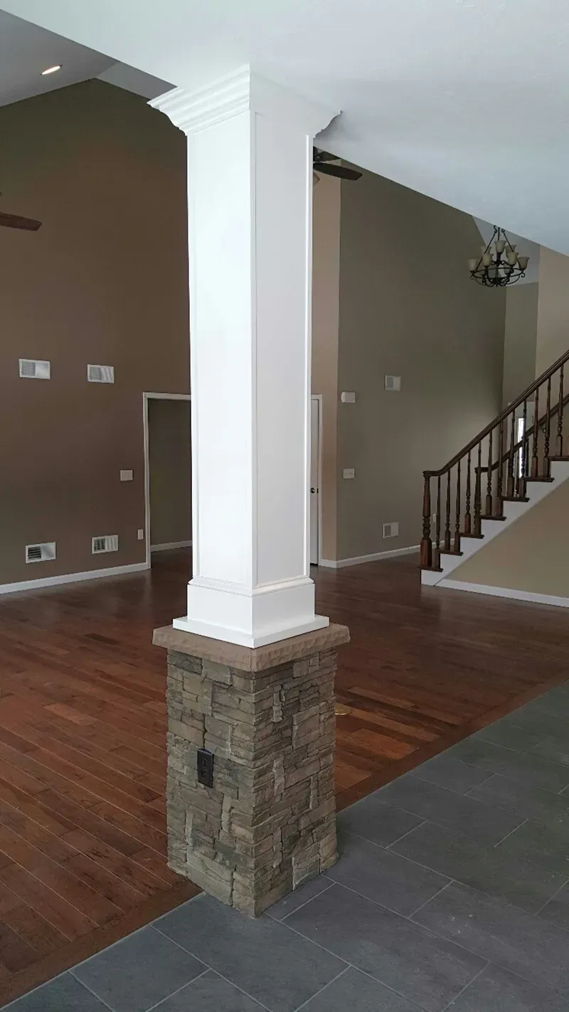 A floor-to-ceiling support column with a stone base and white wooden top in an open-plan home with hardwood floors.
