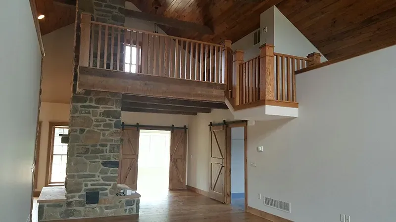 A rustic interior with a stone fireplace, wood-paneled vaulted ceiling, and an open loft balcony overlooking the room.