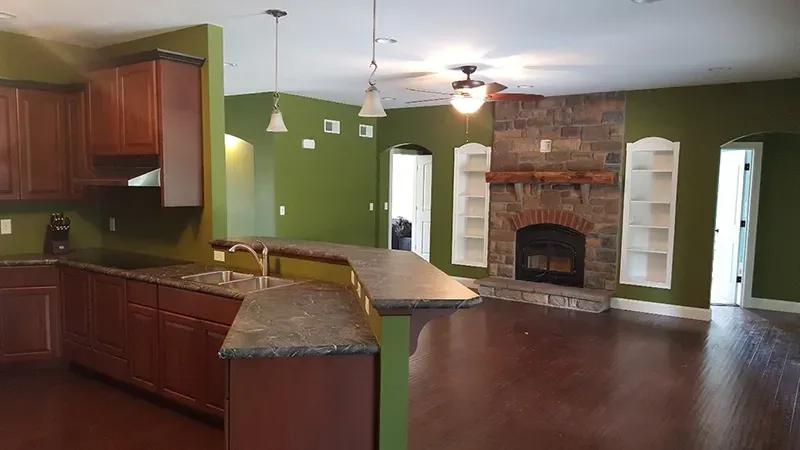 Open-concept kitchen with dark wood cabinets and green walls, featuring a stone fireplace and hardwood floors.