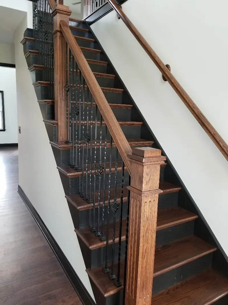 A wooden staircase with dark risers and metal railings set against a plain wall inside a home.