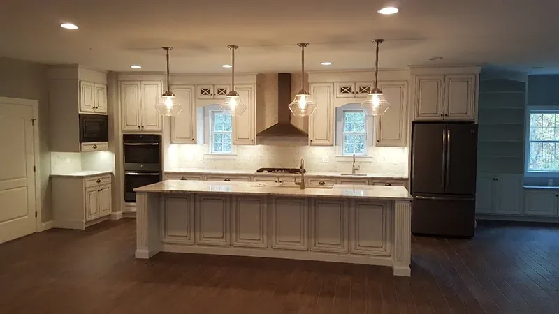 A kitchen with white cabinets, a large island, stainless steel appliances, and four pendant lights hanging above.