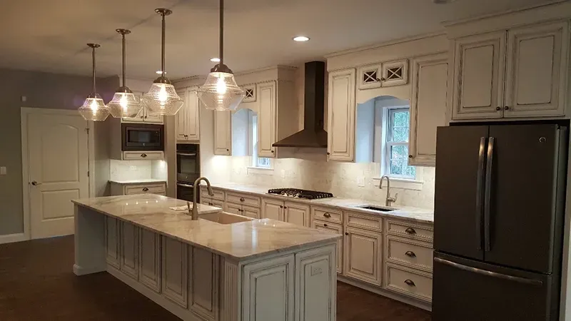 A modern kitchen with white cabinetry, a large marble island, stainless steel appliances, and pendant lighting.