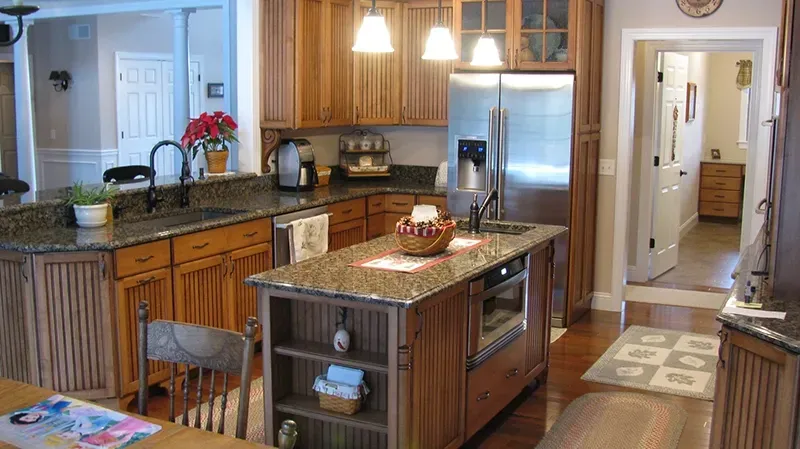 A traditional kitchen with wood cabinets, granite countertops, a central island, stainless steel appliances, and lighting.