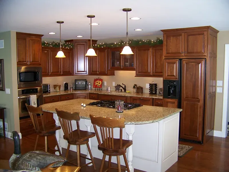 A traditional kitchen with cherry wood cabinets, granite countertops, a center island with three stools, and pendant lights.