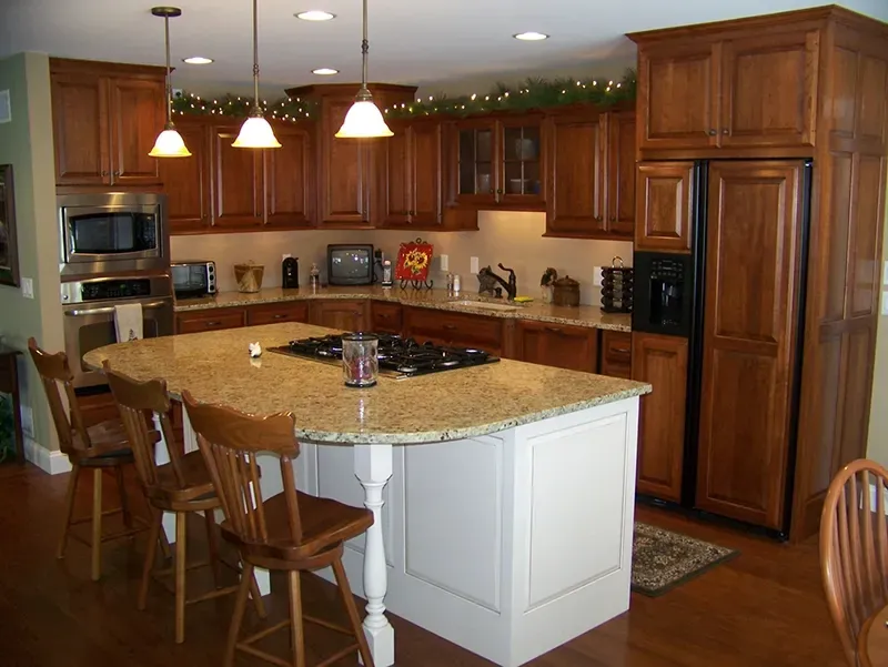 A kitchen with wood cabinets, granite countertops, a central island with bar seating, and recessed and pendant lighting.