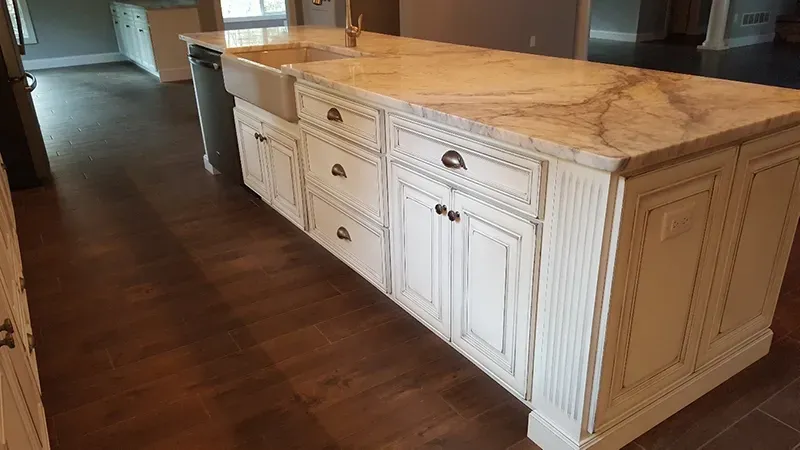 A large, white, vintage-style kitchen island with a stone countertop and farmhouse sink, set on dark wood flooring.