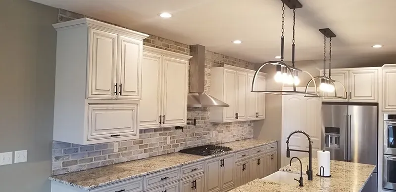 Modern kitchen with white cabinets, granite countertops, a brick backsplash, stainless steel appliances, and island lights.