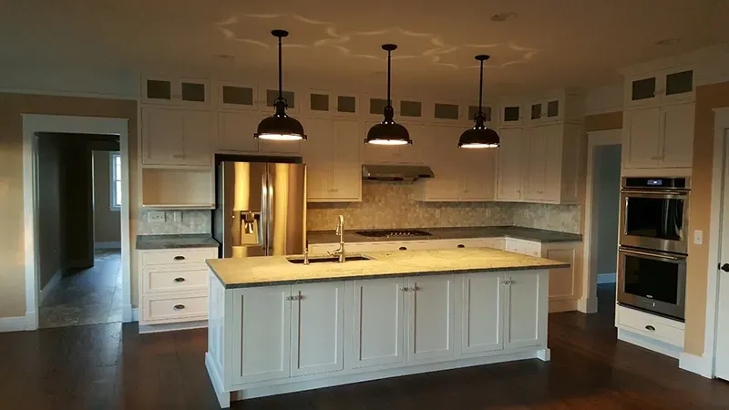 A spacious kitchen with white cabinets, a large central island, stainless steel appliances, and three pendant lights.