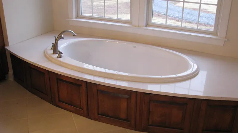 An oval white bathtub set into a white countertop with dark wood paneling below, positioned in front of a window.
