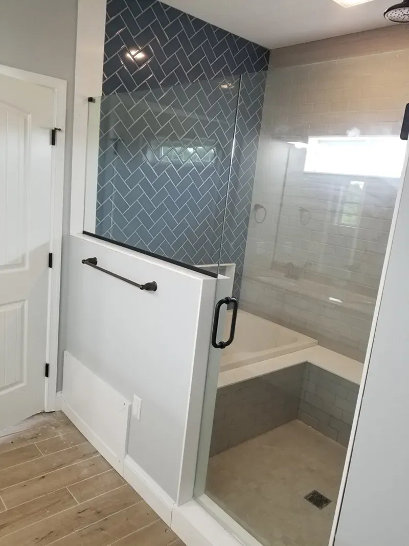 A modern bathroom shower with a partial white wall, glass enclosure, and a blue herringbone-tiled feature wall.