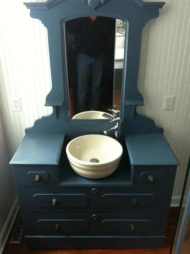 A blue-painted antique dresser repurposed as a bathroom vanity with a white vessel sink, faucet, and attached mirror.