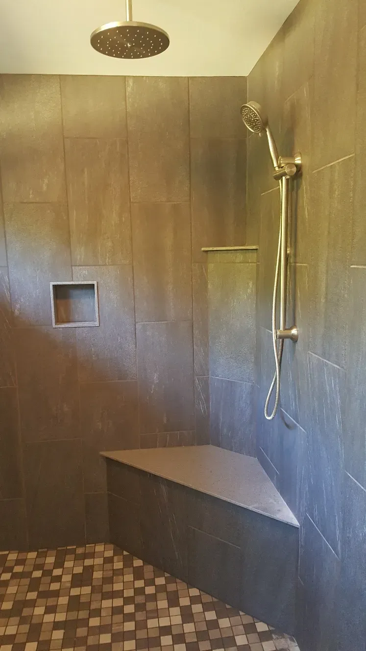 Modern shower with dark stone walls, a square built-in niche, a rainfall head, a handheld sprayer, and a corner seat.
