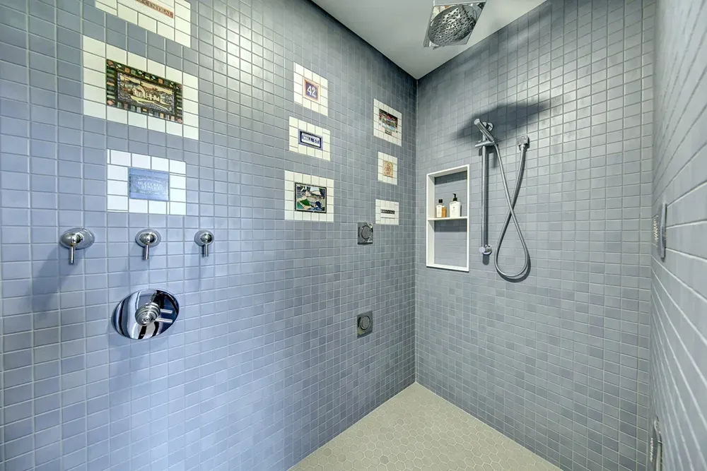 A modern walk-in shower with grey tiled walls, multiple shower heads, and framed art decor.