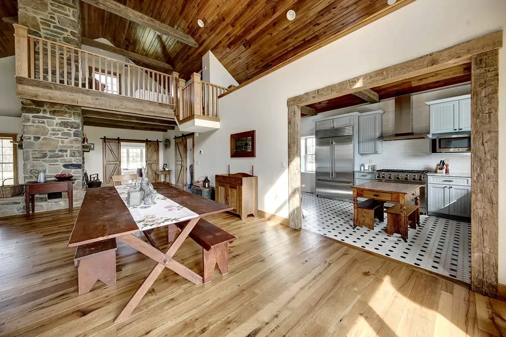 A rustic dining area with a wooden table leads into a kitchen with light cabinets and a patterned tile floor.