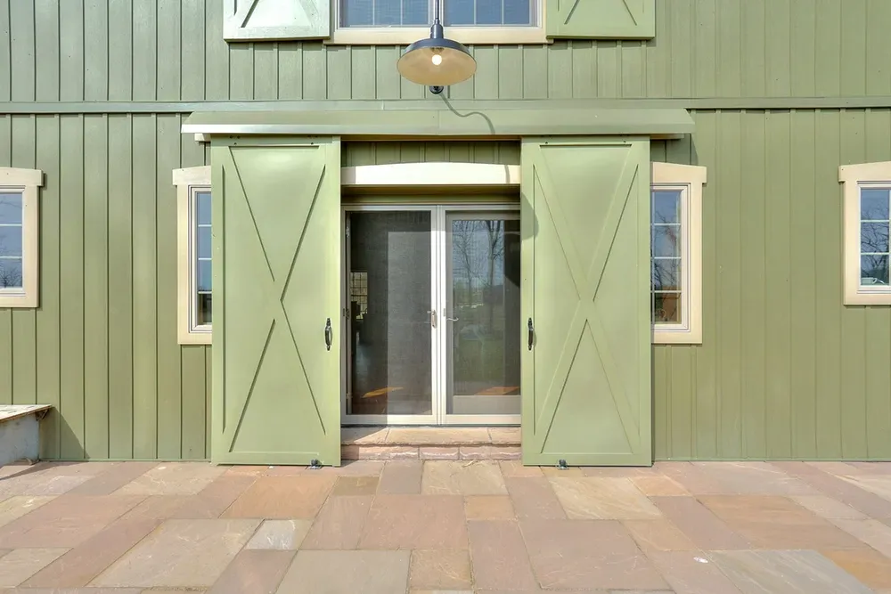 Green barn-style sliding doors flanking a glass-paned doorway on a stone patio.