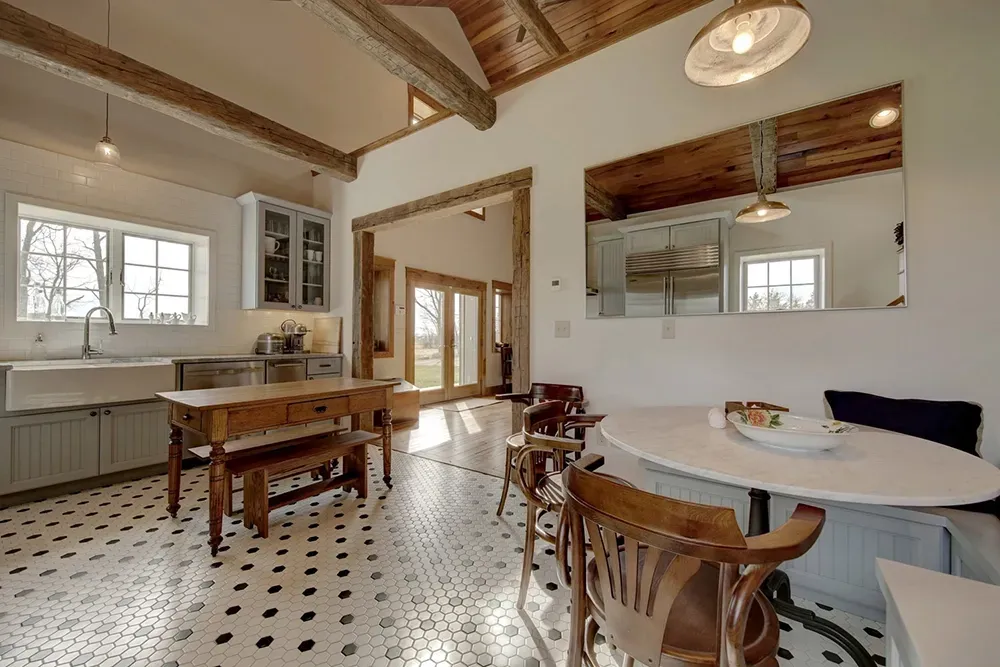 A rustic kitchen and dining space with patterned tile floors, wooden beams, a farmhouse sink, and a round dining table.