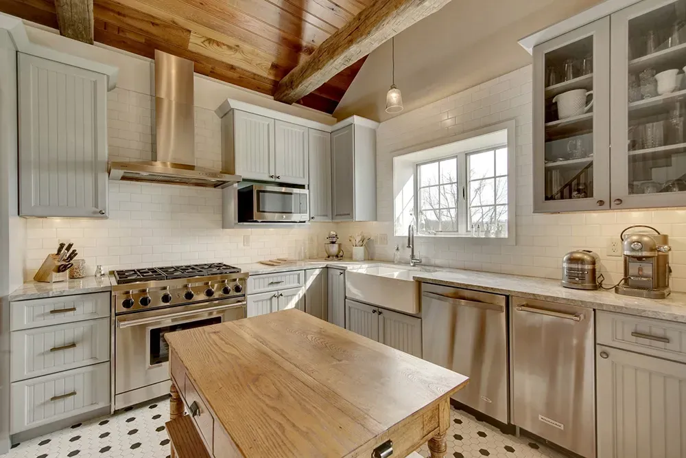 Rustic farmhouse kitchen with light gray cabinetry, stainless steel appliances, a wood-topped island, and white walls.