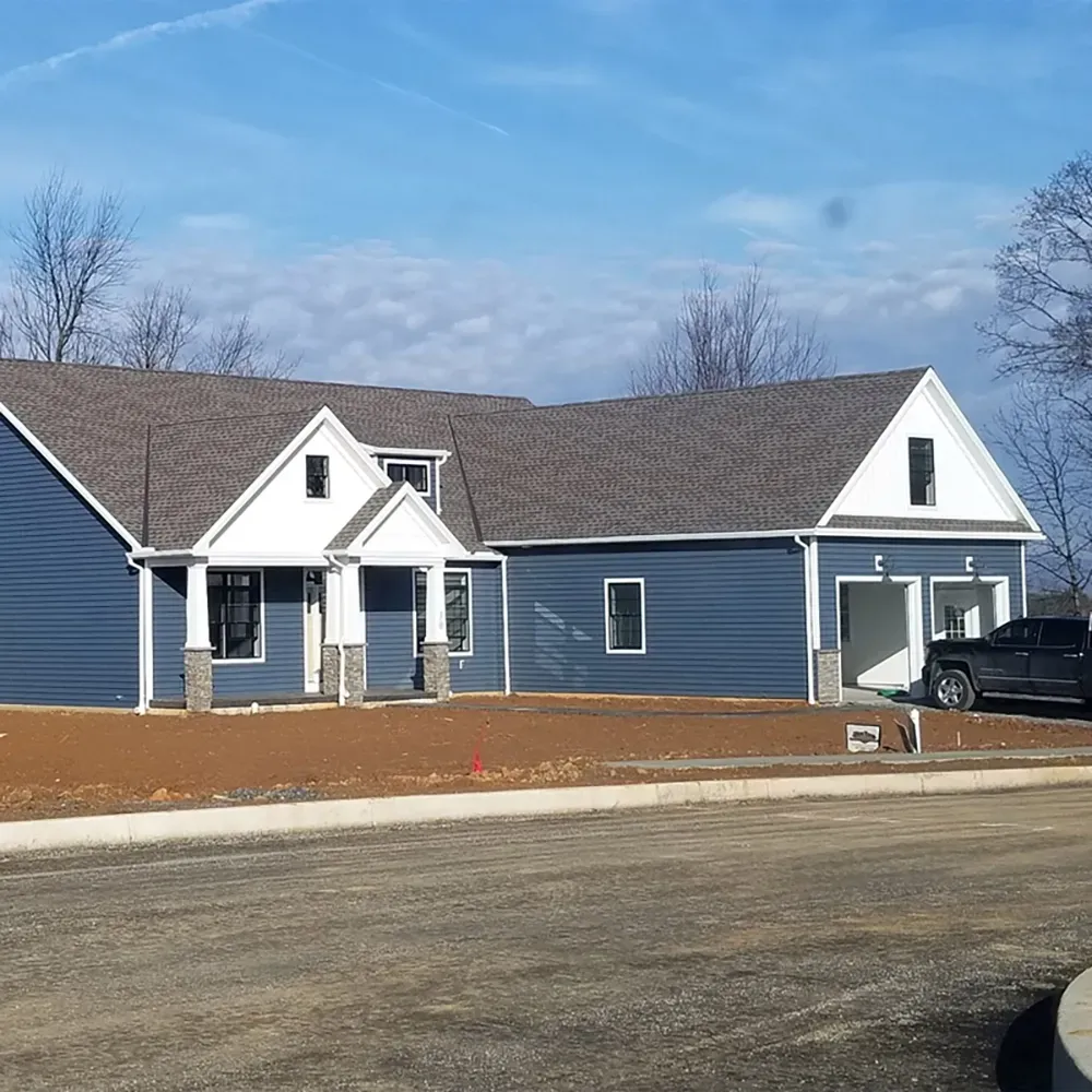 A new single-story house with blue siding, a grey shingled roof, a front porch, and an attached two-car garage.