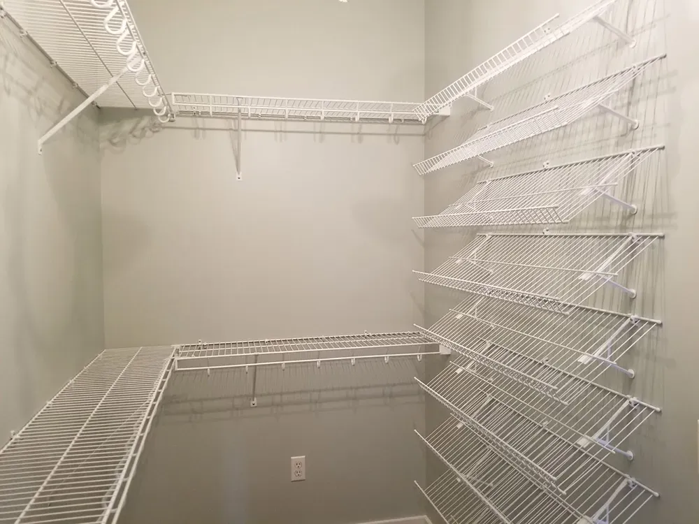 A walk-in closet interior with white wire shelving installed on the walls, including a corner shoe rack and hanger rods.