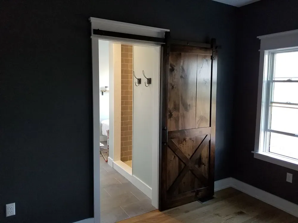 A wooden X-brace sliding barn door separates a dark-walled bedroom from a tiled bathroom.